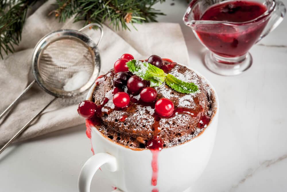 Pocukrovaný čokoládový mugcake v bílém hrníčku s brusinkami a lístkem máty